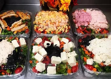 An assortment of catering platters with cured meats, cheeses, vegetables, and olives.